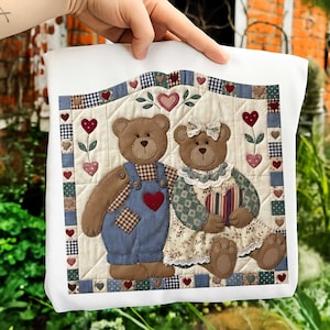 Könnte beinhalten: Ein weißes Kissen mit einem gesteppten Design mit zwei Teddybären. Einer trägt eine blaue Latzhose mit einem roten Herz, der andere ein Blumenkleid. Das Design umfasst Herzen und einen Vichy-Rand.