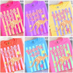 May include: A collection of six crew neck t-shirts in various colors, each featuring a kangaroo illustration and the text "Toodle-Loo". The shirts have vertical striped backgrounds and star accents.