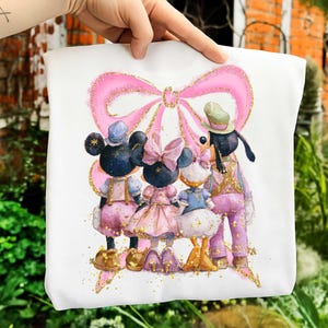 May include: White tote bag featuring a watercolor illustration of Disney characters. The design includes Mickey and Minnie Mouse, Daisy Duck, and Goofy, all dressed in pink and gold outfits, with a large pink bow.