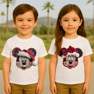 May include: Two white t-shirts featuring Mickey and Minnie Mouse designs with plaid accents and Santa hats. The Mickey Mouse design has a Santa hat, while the Minnie Mouse design has a plaid bow. Both shirts are short-sleeved.