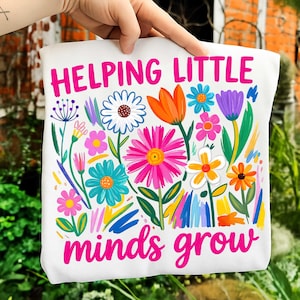 May include: White tote bag with a colorful floral design and the text "Helping Little Minds Grow" in bright pink. The flowers include daisies, tulips, and other blooms in shades of pink, orange, blue, and yellow.