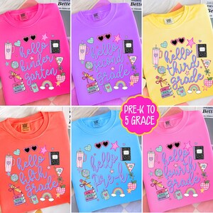 May include: A collection of six crewneck sweatshirts in pink, purple, yellow, orange, and blue, each featuring school-themed graphics including a notebook, pencil, globe, apple, and rainbow, with text reading hello kindergarten, second, third, fourth, fifth grade, or pre-k.