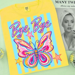 May include: Yellow t-shirt with a colorful butterfly graphic and the words "Bye Bye" in pink script. The butterfly has pink, orange, and blue details. The shirt also features blue vertical stripes and star accents.