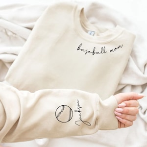 May include: Beige sweatshirt with the text "baseball mom" on the front and a baseball with the name "Jackson" on the sleeve.