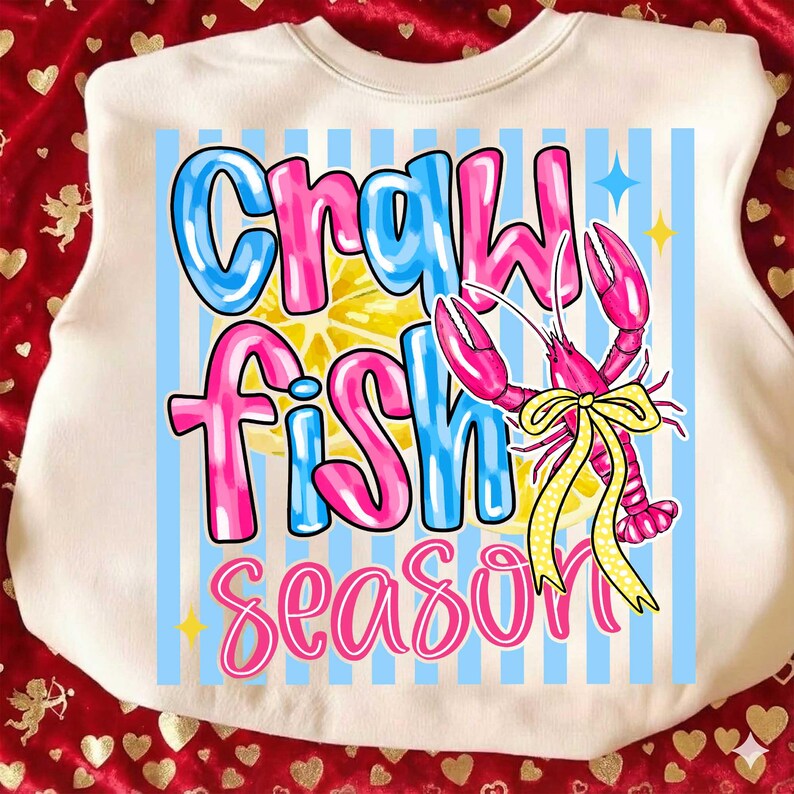 May include: Cream-colored sweatshirt with a graphic design. The design features the words "Crawfish Fish Season" in blue and pink, a pink crawfish with a yellow bow, and a lemon slice. Blue vertical stripes are in the background.