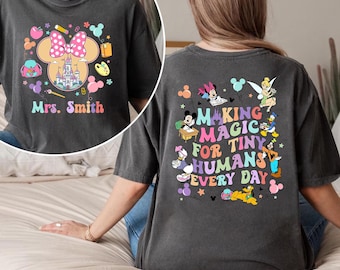 Puede incluir: Camiseta gris oscuro con un diseño de Minnie Mouse y el texto "Mrs. Smith" en la parte delantera. La parte trasera de la camiseta tiene el texto "Making Magic for Tiny Humans Every Day" con personajes de Disney.