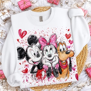 以下が含まれることがあります： ミッキーマウス、ミニーマウス、グーフィーの水彩イラストが描かれた白いクルーネックのスウェットシャツ。赤いハートとペイントのスプラッシュが特徴で、遊び心のあるテーマを演出しています。袖は長く、カフスが付いています。