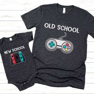 以下が含まれることがあります： ビデオゲームコントローラーのグラフィックが描かれたグレーのTシャツ2枚。大きい方のTシャツには「OLD SCHOOL」、小さい方のTシャツには「NEW SCHOOL」と書かれています。