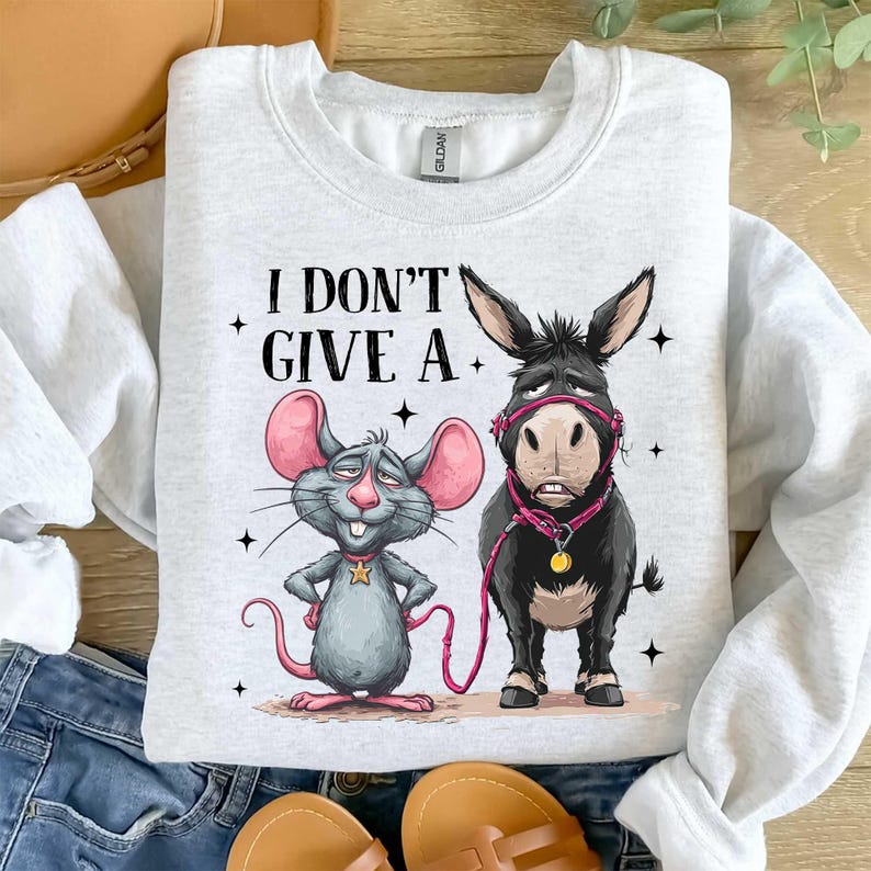 Puede incluir: Una sudadera gris claro con un rat&oacute;n y un burro de dibujos animados y el texto "I DON'T GIVE A." El rat&oacute;n es gris con orejas rosas y un collar de estrella. El burro es negro con un cabestro rosa.