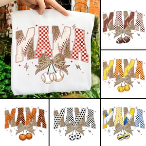 Puede incluir: Sudadera blanca con la palabra "MAMA" en un diseño retro. Las letras tienen una puntada de béisbol y un patrón de cuadros rojos. Un lazo con estampado de leopardo y pelotas de béisbol completan el diseño. La sudadera es sostenida por una mano.