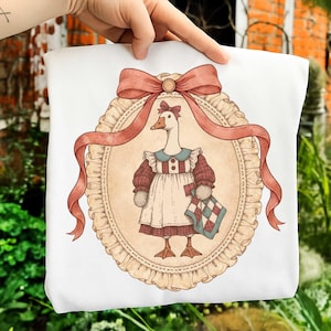 May include: White cushion cover with a charming illustration of a goose in a vintage dress. The goose is within an oval frame, adorned with a red ribbon and bow. The goose holds a small, checkered blanket.
