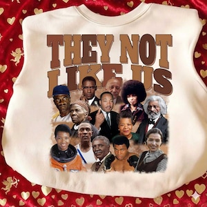 May include: A cream-coloured sweatshirt with the text "THEY NOT LIKE US" in brown block letters. Below the text is a collage of historical figures. The graphic includes portraits of notable individuals.