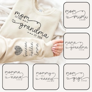 Könnte beinhalten: Ein beiger Pullover mit dem Text "mom est 1982 grandma est 2024" auf der Vorderseite und den Namen "Gannon, Holden, Emma" auf dem Ärmel. Der Pullover wird mit anderen Pullovern mit ähnlichen Designs gezeigt, darunter "mom est mimi", "mama est grandma", "momma est nana", "mommy est nanny" und "mom est gigi".