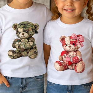 Könnte beinhalten: Weiße T-Shirts mit Teddybären-Designs. Ein Bär ist in Tarnfarben mit einer Kappe und hält ein Herz mit "LOVE" darauf. Der andere Bär ist rot und rosa mit einer Schleife und hält ebenfalls ein Herz mit "LOVE" darauf. Die Shirts werden von Kindern getragen.