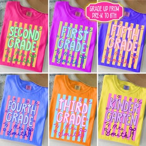 May include: A collection of colorful t-shirts, each displaying a different grade level from kindergarten to fifth grade. The shirts feature bold text, stars, and the name "Mrs. Smith". The shirts are in various colors, including pink, purple, blue, orange, and yellow.