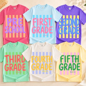 May include: Six short-sleeve crew neck t-shirts in pink, light blue, purple, light green, white, and yellow. Each shirt features vertical stripes and bold text reading PRE SCHOOL, FIRST GRADE, SECOND GRADE, THIRD GRADE, FOURTH GRADE, and FIFTH GRADE.