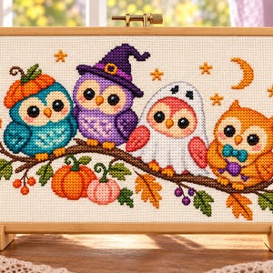 Puede incluir: Un bordado de punto de cruz rectangular en un marco de madera que muestra cuatro búhos sobre una rama. Los búhos llevan disfraces de Halloween, incluyendo un sombrero de calabaza, un sombrero de bruja morado, una sábana de fantasma y una pajarita azul.