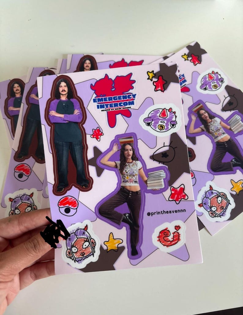 May include: A set of stickers featuring cartoon characters, stars, and a red logo that says "Emergency Intercom" with the text "Headed by Marc Jacobs". The stickers are on a purple background with brown and white accents.
