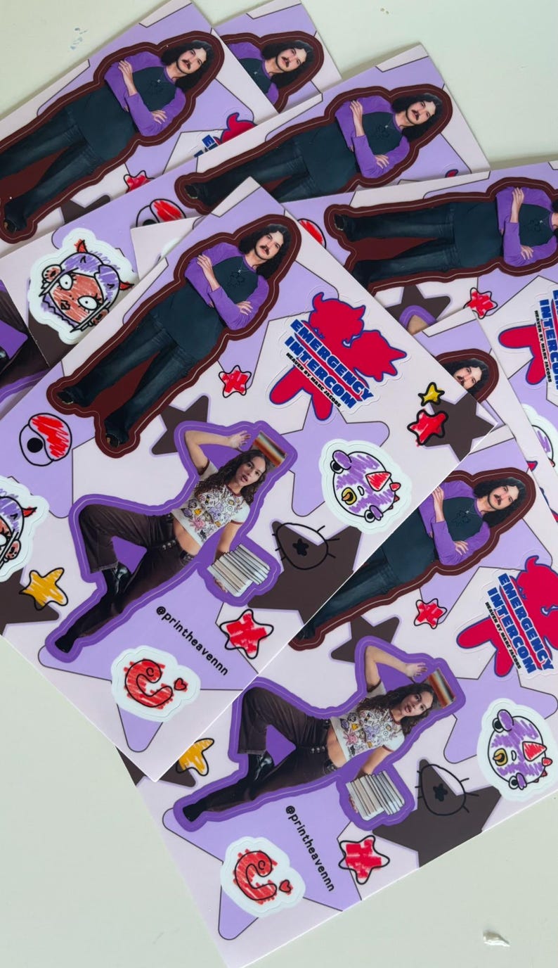 May include: A set of stickers featuring a cartoon character with a purple and pink colour scheme. The stickers are on a purple background with white stars and the text "Emergency Intercom" in a red and white font. The stickers are designed for use on laptops, water bottles, and other surfaces.