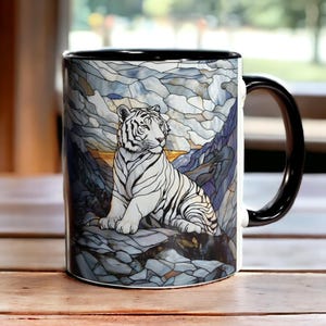 Puede incluir: Taza de cer&aacute;mica con asa y borde negros. La taza presenta una ilustraci&oacute;n de tigre blanco sobre un fondo de dise&ntilde;o de vidrieras azules, grises y amarillas. La taza est&aacute; sobre una superficie de madera.