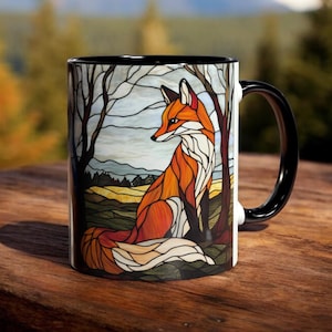 Peut inclure: Une tasse à café en céramique avec un bord et une poignée noirs. La tasse présente un motif de vitrail représentant un renard roux assis dans un décor forestier.