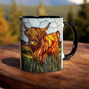 May include: A white ceramic mug with a black rim and handle. The mug features a stained glass design of a Highland cow with brown, orange, and yellow colors.