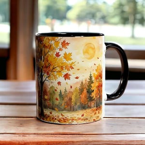 Peut inclure: Une tasse en céramique avec une anse et un intérieur noirs. La tasse présente une peinture à l'aquarelle d'une scène d'automne avec un arbre, des feuilles qui tombent et un soleil jaune. La tasse est posée sur une surface en bois.