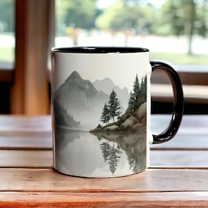 May include: White ceramic mug with a black interior and handle. The mug features a landscape design of mountains, trees, and a lake, with reflections in the water. The design is in shades of gray and white.