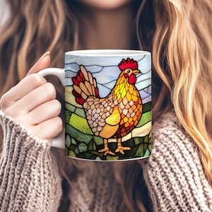 May include: White ceramic mug with a stained-glass effect rooster design. The rooster is depicted in red, yellow, and orange hues, set against a green and blue backdrop. The mug is held by someone wearing a grey jumper.