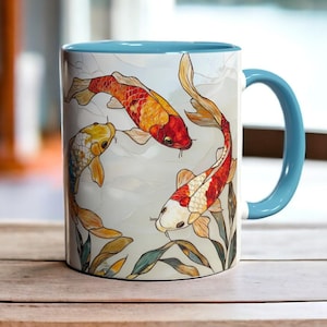 Może przedstawiać: Biały kubek ceramiczny z niebieskim rantem i uchwytem przedstawia kolorową ilustrację trzech karpi koi pływających w kółko. Ryby są pomarańczowe, czerwone, białe i czarne.