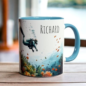 May include: A white ceramic mug with a blue rim and handle. The mug features a colorful illustration of a scuba diver swimming through a coral reef with the name "RICHARD" printed on the side.