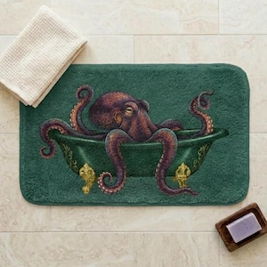 May include: A green bath mat depicts a purple octopus in a green bathtub with gold detailing. A white towel and a wooden soap dish with a bar of purple soap are also present.