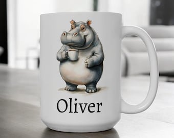 May include: White ceramic mug with a cartoon illustration of a gray hippopotamus holding a cup of coffee. The mug has the name "Oliver" printed on the bottom.