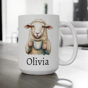 Könnte beinhalten: Weiße Keramik-Kaffeetasse mit einer Cartoon-Illustration eines Schafs, das eine Tasse Kaffee hält. Die Tasse trägt den Namen "Olivia" auf der Unterseite.