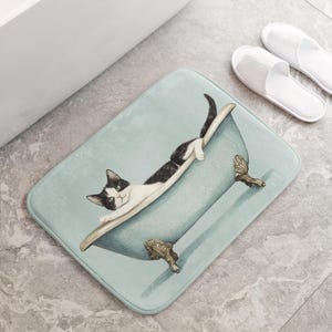 Peut inclure: Un tapis de bain bleu et blanc avec un chat noir et blanc dans une baignoire. Le chat regarde l'appareil photo.