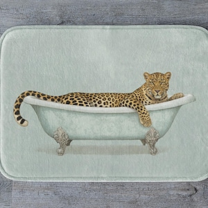 May include: A rectangular bath mat featuring a leopard relaxing in a vintage-style bathtub. The leopard has a spotted coat and is lying in a light blue tub with ornate feet. The mat has a light green background.