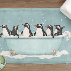 May include: A light blue bath mat with a charming illustration of six penguins in a bathtub. The penguins are black and white with orange beaks, and the tub has seashell accents. A white towel and sandals are also visible.