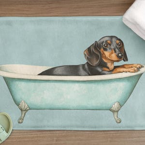 Może przedstawiać: Czarno-brązowy pies rasy dachshund siedzi w jasnoniebieskiej wannie na jasnoniebieskiej macie łazienkowej. Pies patrzy w obiektyw.