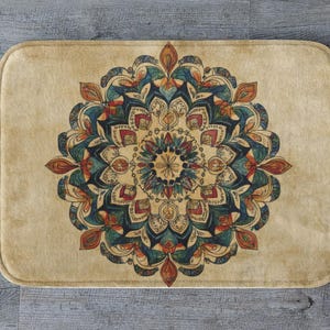 Puede incluir: Alfombra de baño rectangular beige con un diseño de mandala detallado en tonos turquesa, rojo y naranja. El patrón floral está centrado en la alfombra, creando un elemento simétrico y decorativo. La alfombra tiene esquinas redondeadas.