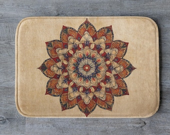 May include: A rectangular beige bath mat featuring a detailed mandala design in shades of red, orange, blue, and cream. The floral pattern is centered on the mat, creating a symmetrical design. The mat has rounded corners.