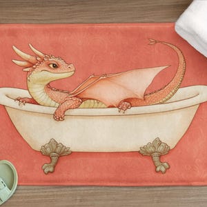Puede incluir: Un dragón rojo con alas está tomando un baño en una bañera blanca con patas doradas. La bañera está sobre una alfombra de baño rosa.