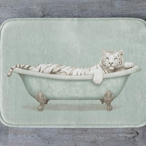May include: A rectangular bath mat featuring a watercolour illustration of a white tiger in a vintage bathtub. The mat has a light green background and a grey wooden floor.