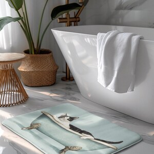 Peut inclure: Un tapis de bain bleu clair avec un chat noir et blanc dans une baignoire. Le chat est allong&eacute; dans la baignoire, la t&ecirc;te pos&eacute;e sur le bord. La baignoire a des pieds dor&eacute;s.