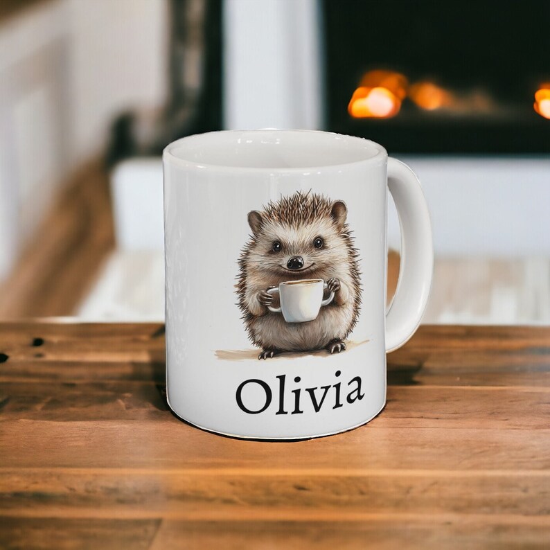 May include: White ceramic mug with a cartoon hedgehog holding a cup of coffee. The mug has the name "Olivia" printed on the bottom.