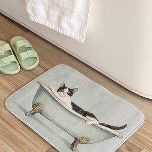 Peut inclure: Un tapis de bain bleu clair avec un chat noir et blanc dans une baignoire. Le chat est allong&eacute; dans la baignoire, la t&ecirc;te pos&eacute;e sur le bord. La baignoire a des pieds dor&eacute;s.