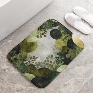 May include: A rectangular bath mat with a watercolour design of green foliage and abstract shapes. The mat has a light grey background with a border of dark green. White slippers are next to the mat.