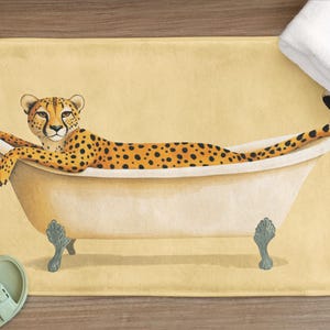 Peut inclure: Un tapis de bain jaune avec un guépard dans une baignoire blanche. Le guépard est allongé sur le dos, les pattes en l'air. La baignoire a deux pieds argentés.
