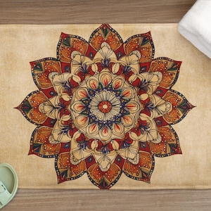 Puede incluir: Una alfombra de baño beige con un diseño de mandala detallado en tonos rojos, naranjas y azules. La alfombra es rectangular con esquinas redondeadas. También se ven una toalla blanca y un par de sandalias verde claro.