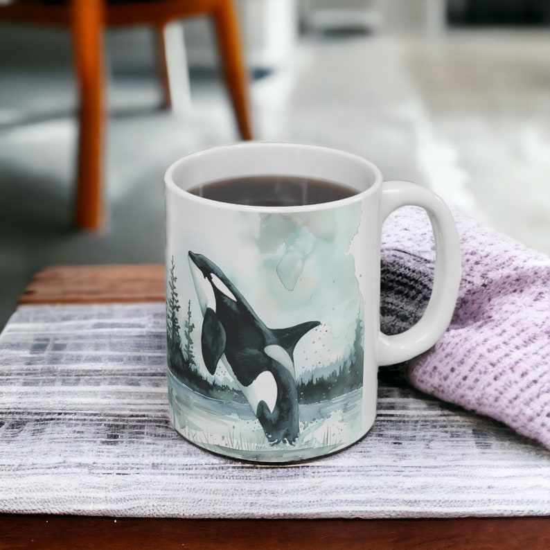 May include: White ceramic mug with a black and white watercolor illustration of an orca jumping out of the water. The mug is filled with coffee.