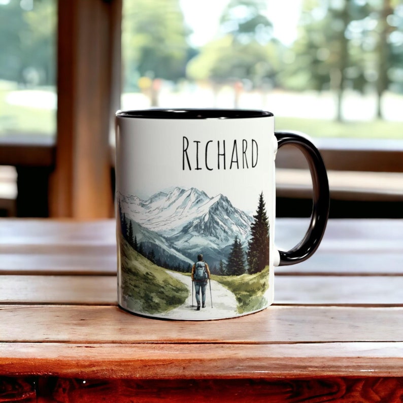 May include: White ceramic mug with a black rim and handle. The mug features a watercolour illustration of a hiker walking on a path through a mountain landscape. The name "RICHARD" is printed in black at the top of the mug.